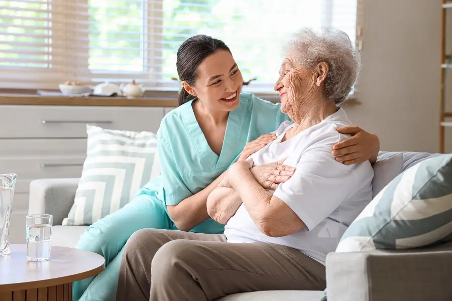 Caregiver hugging a smiling older woman on a sofa