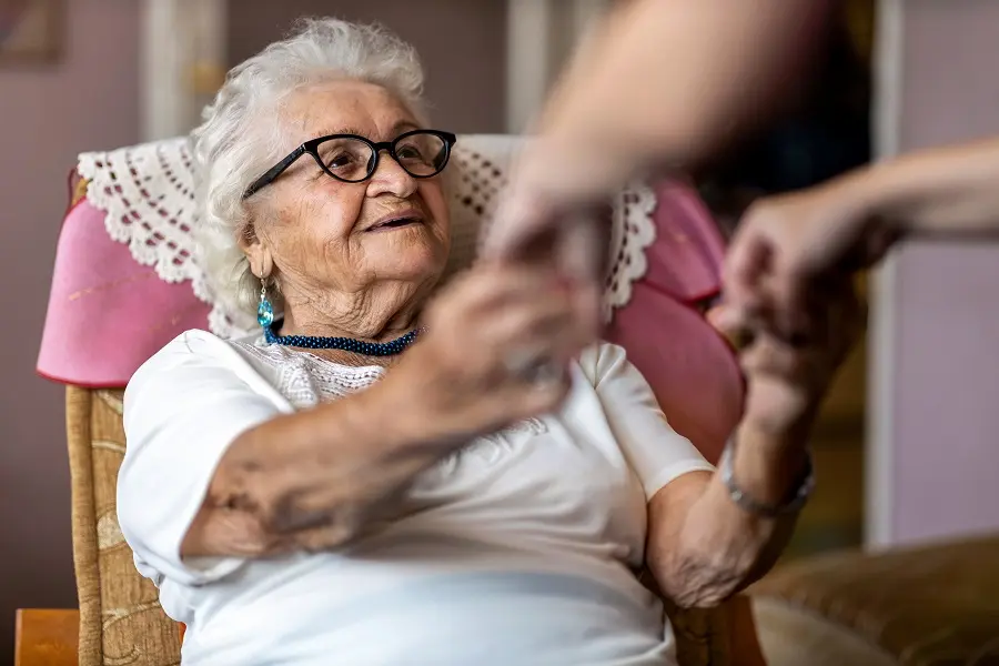 Caregiver holding the hands of a smiling older woman in glasses