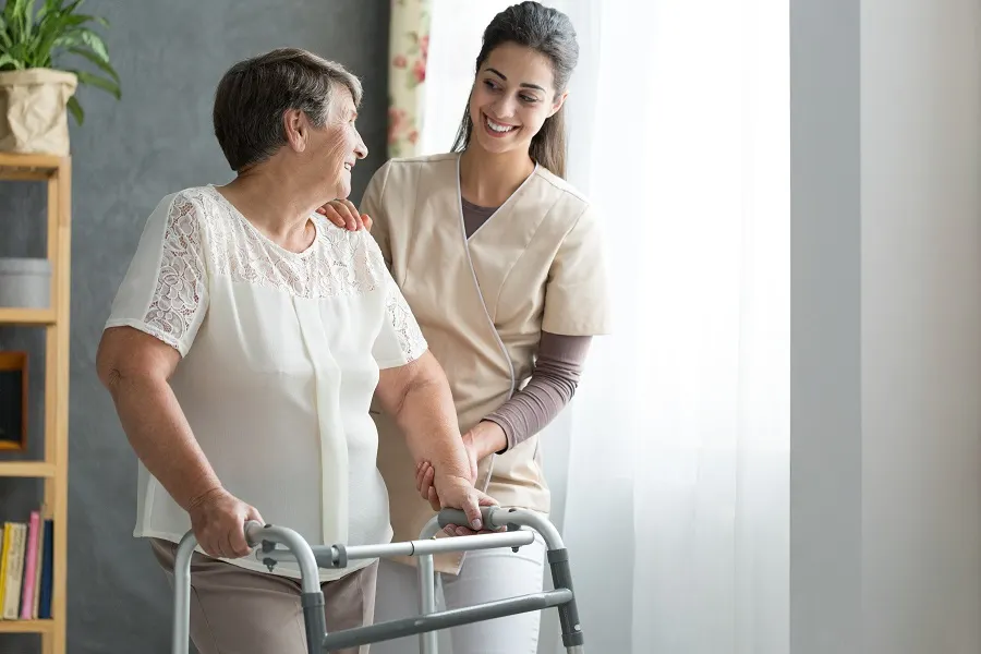Caregiver helping an older woman walk with a walker