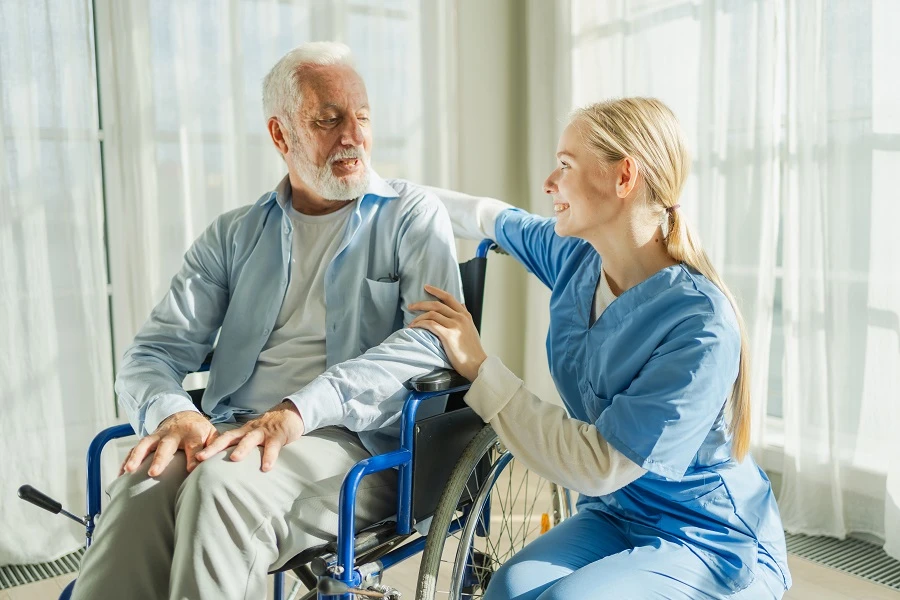 Nurse kneeling beside a smiling older man in a wheelchair