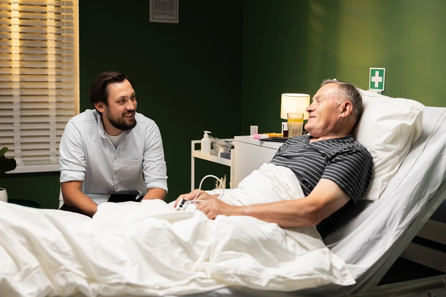 Man sitting beside an older man resting in a hospital bed