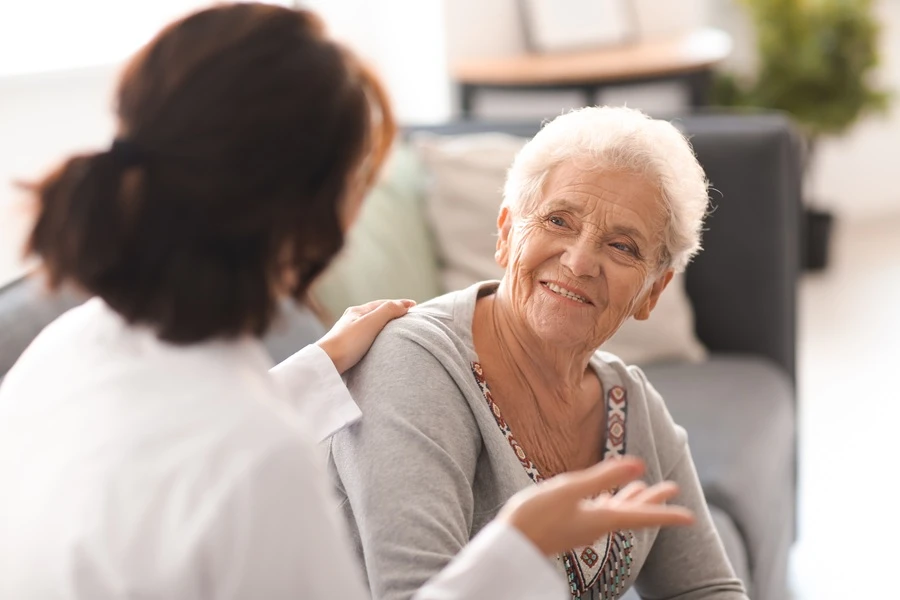 Caregiver talking with a smiling older woman on a sofa