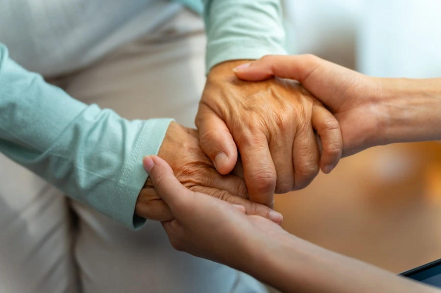 Close-up of a caregiver holding an older person's hands