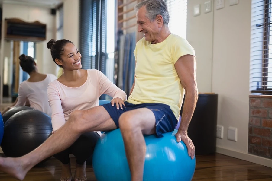 Physical therapist helping an older man exercise on a stability ball