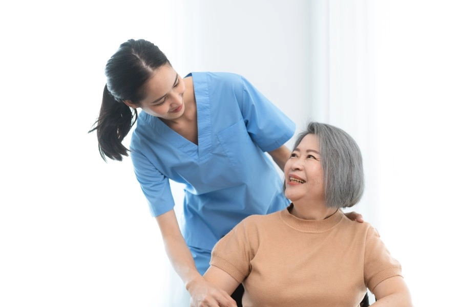 Nurse in blue scrubs leaning over a smiling older woman in a wheelchair