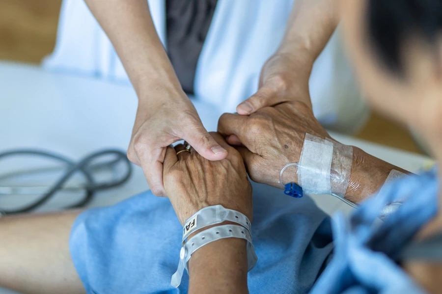Caregiver holding the hands of a patient wearing a hospital wristband