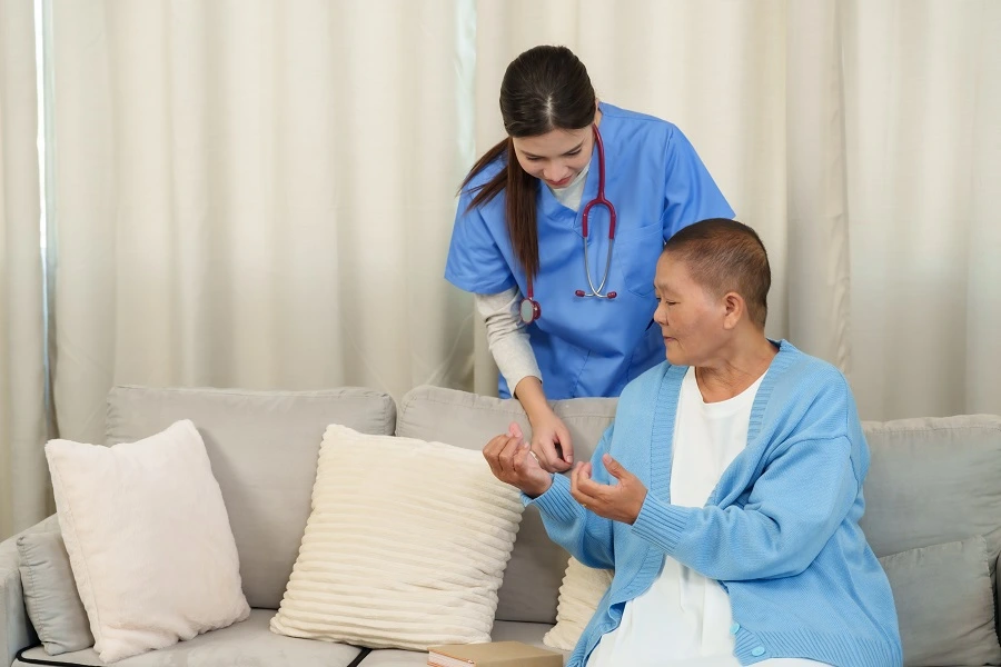 Nurse helping an older woman on a sofa at home