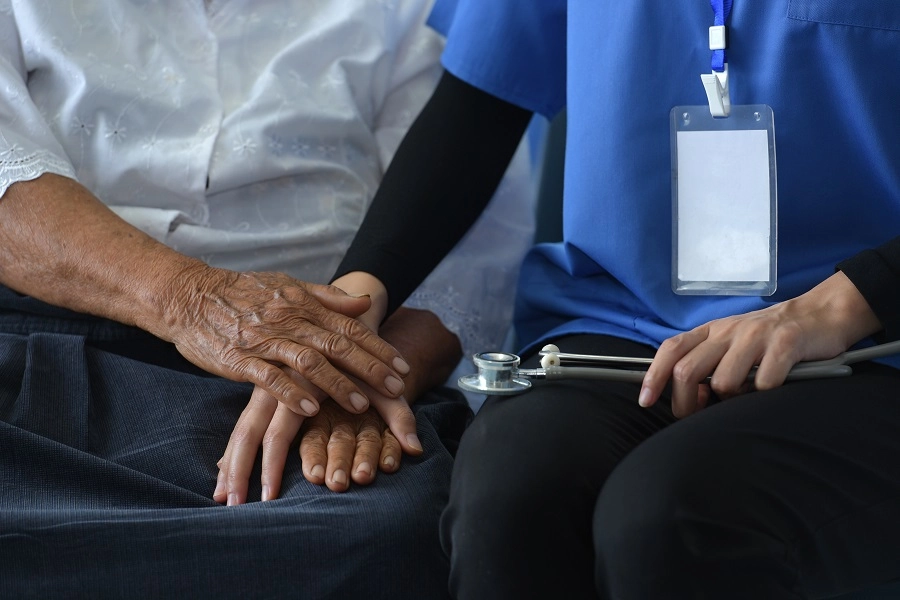 Nurse in scrubs resting her hand on an older patient's hands