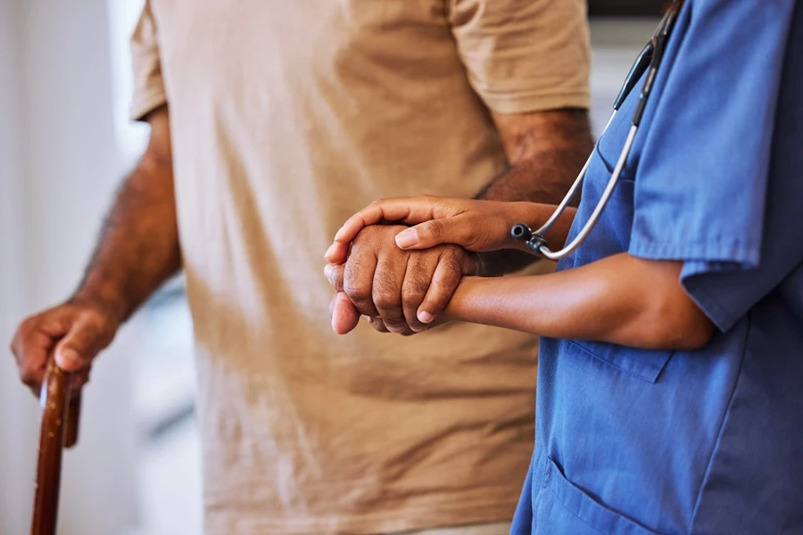 Nurse holding the hand of an older man with a cane