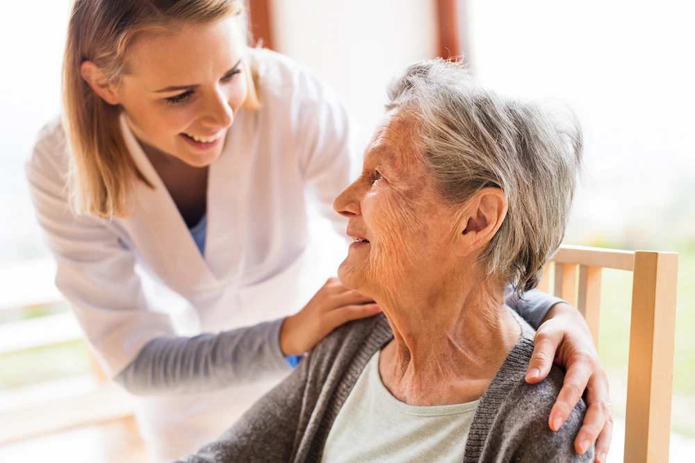Una cuidadora sonriente con las manos sobre los hombros de una anciana.
