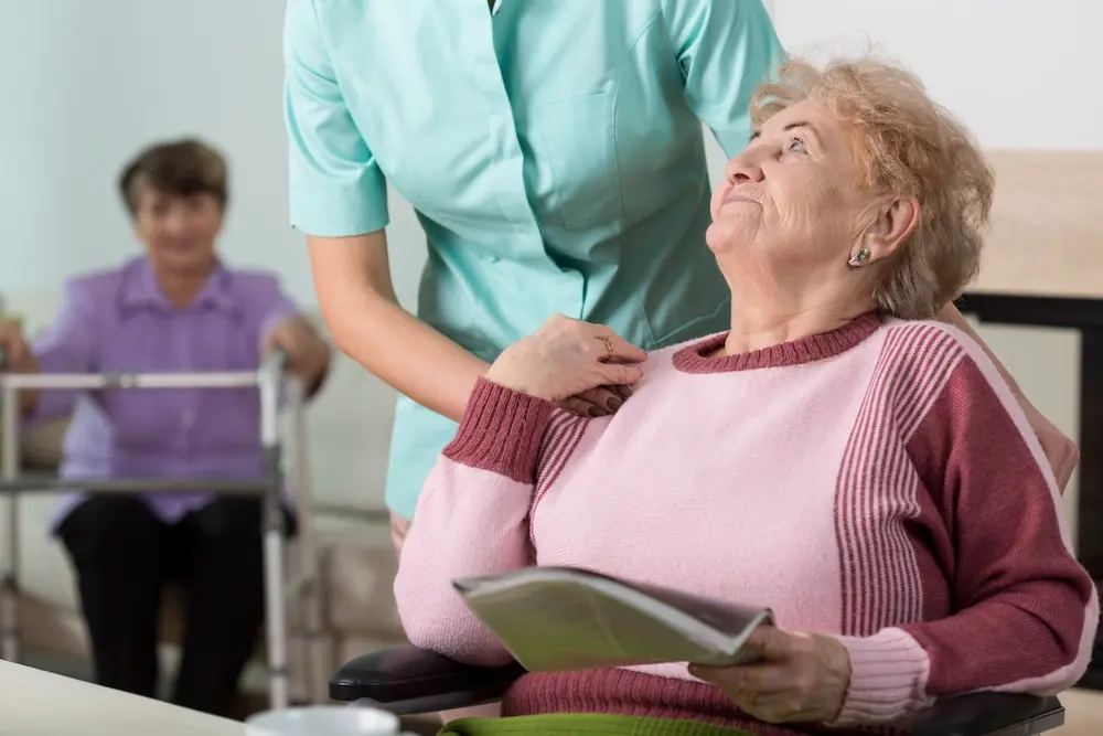 Una cuidadora con la mano sobre el hombro de una anciana sonriente.
