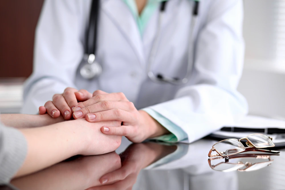 Médico sosteniendo las manos de un paciente sobre un escritorio.