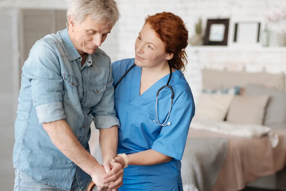 Nurse helping an older man walk at home