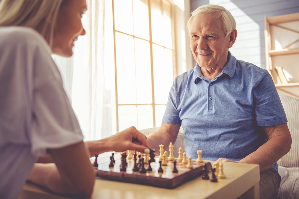 Cuidadora jugando al ajedrez con un anciano sonriente.