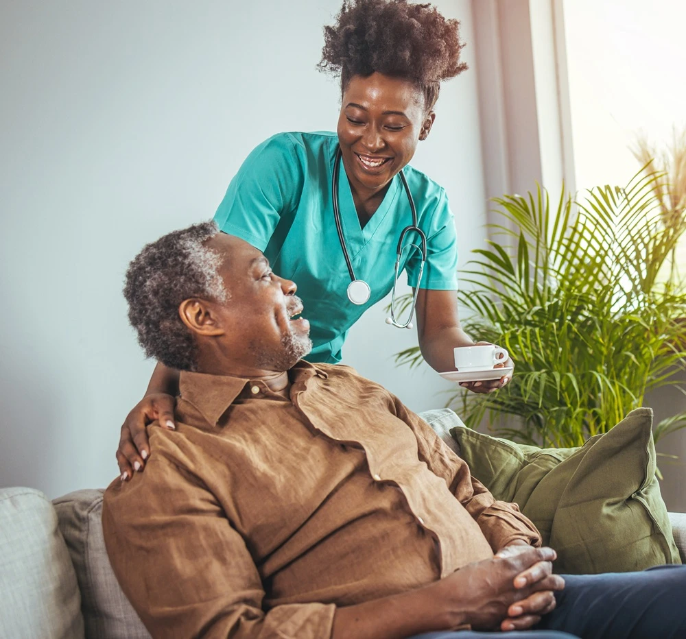 Nurse bringing a cup to an older man sitting on a sofa