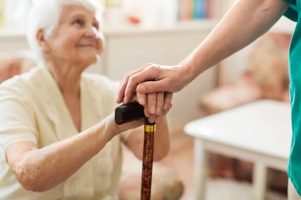 Caregiver steadying an older woman's hand on her cane