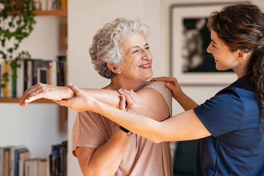 Caregiver helping a smiling older woman stretch her arms