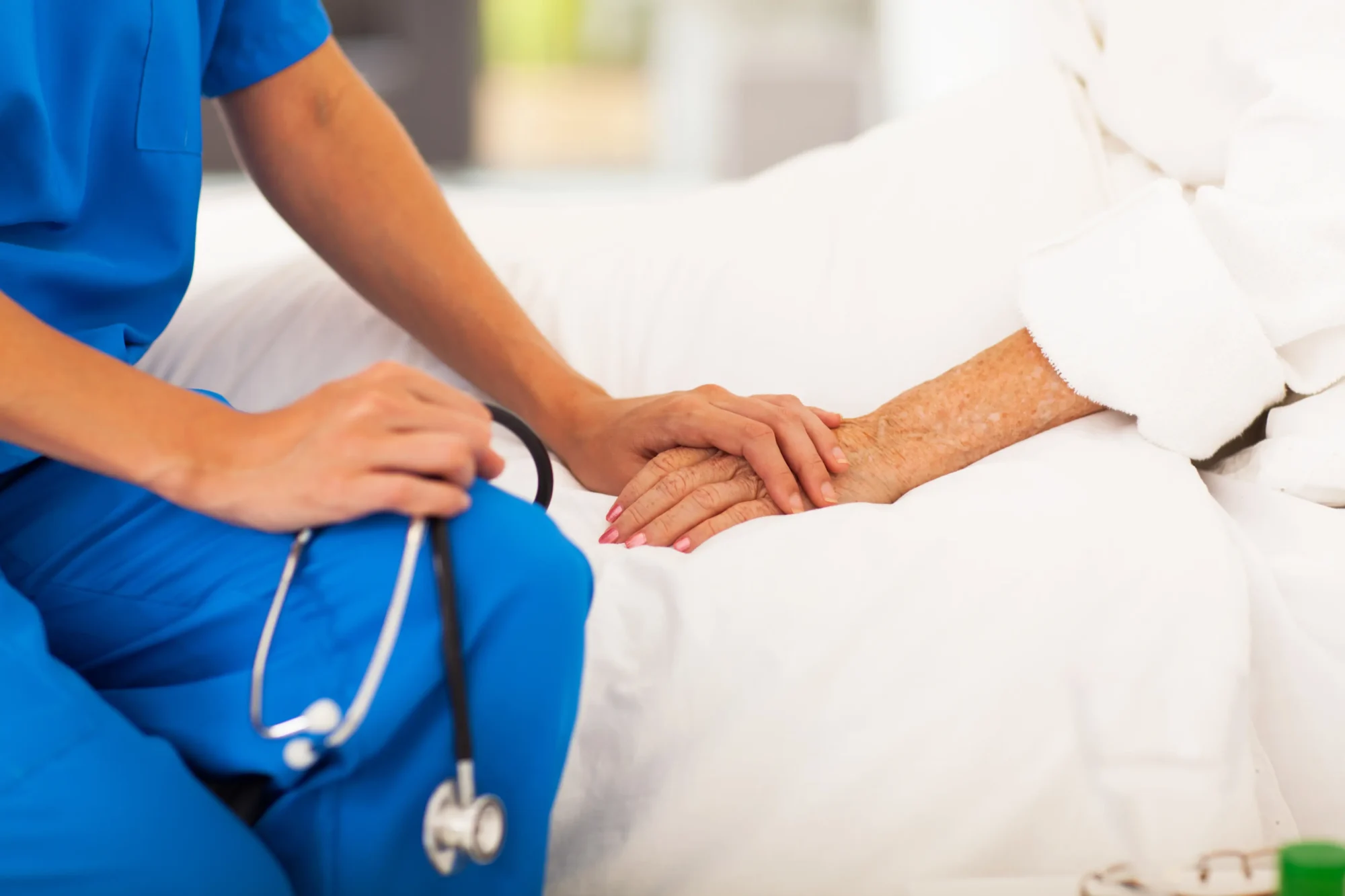 Enfermera con estetoscopio sosteniendo la mano de un paciente en la cama.
