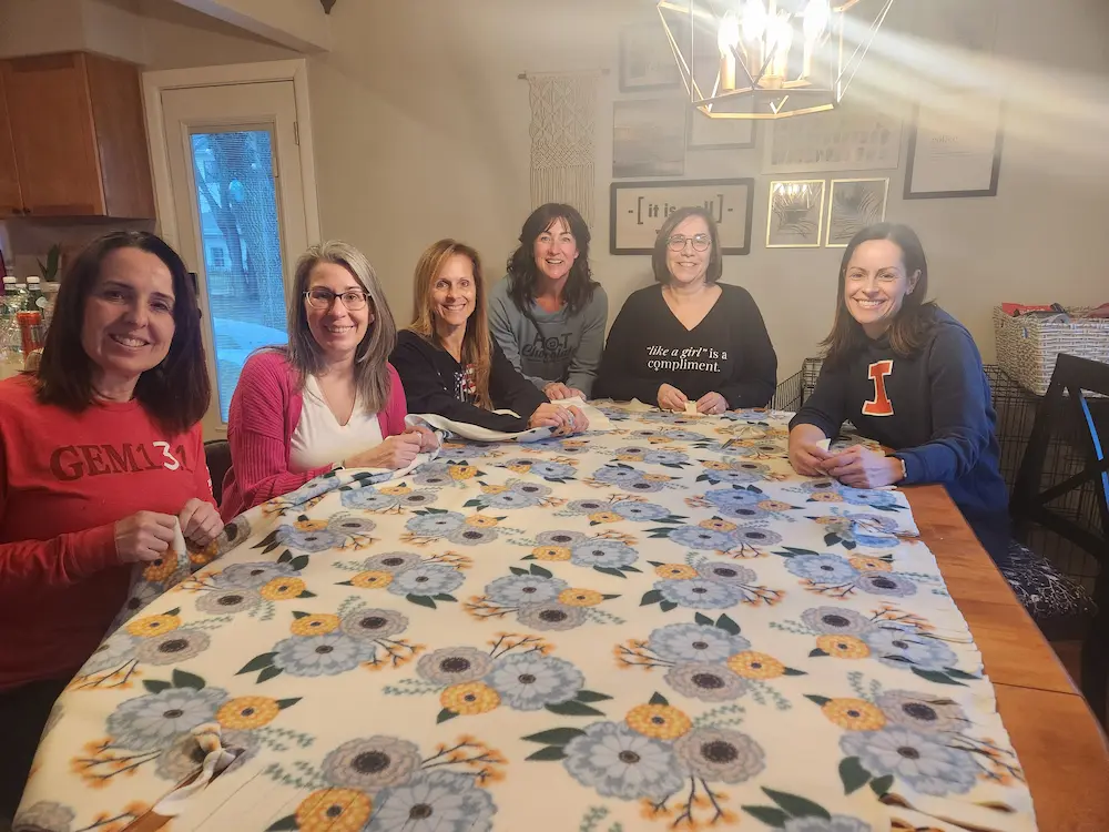 Voluntarios de APEX alrededor de una mesa con una colcha hecha a mano.